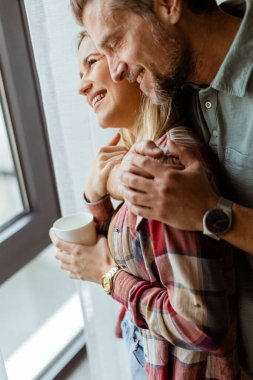 Hafifçe aydınlatılmış bir odada, bir erkek, bir kadına arkadan sarılır. İkisi de pencereden dışarı bakar, birlikte sakin ve samimi bir anı paylaşırlar.