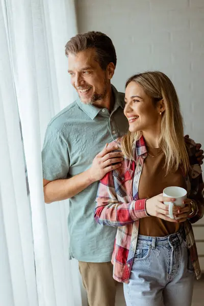 Hafifçe aydınlatılmış bir odada, bir erkek, bir kadına arkadan sarılır. İkisi de pencereden dışarı bakar, birlikte sakin ve samimi bir anı paylaşırlar.