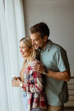 Hafifçe aydınlatılmış bir odada, bir erkek, bir kadına arkadan sarılır. İkisi de pencereden dışarı bakar, birlikte sakin ve samimi bir anı paylaşırlar.