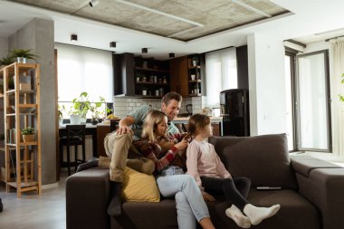 Aile kanepede rahat bir anın tadını çıkarır, neşeli etkileşimler ve sıcak gülümsemelerle.