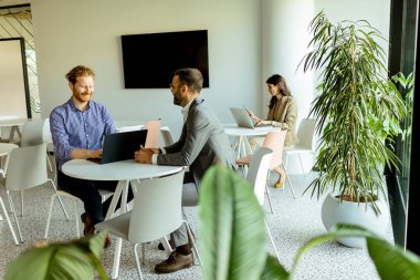 Modern bir masada dizüstü bilgisayar üzerinde çalışırken derin tartışmalara giren iki adam..