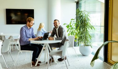 Modern bir masada dizüstü bilgisayar üzerinde çalışırken derin tartışmalara giren iki adam..