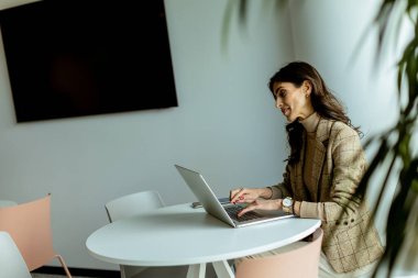 Profesyonel bir kadın şık, güneşli bir kafede dizüstü bilgisayardaki işine odaklanmış.
