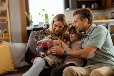 Neşeli ebeveynler, kızlarının evde mutlu bir buldogla oynamasını izliyorlar.