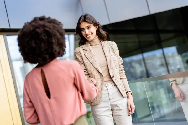 Stock image Two women engage in a friendly handshake, one laughing joyously, symbolizing a positive business interaction.