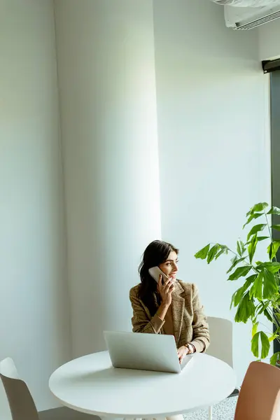 女性は 彼女の横にラップトップと緑の植物と思考で失われた日光のオフィスで白いテーブルに座っています — ストック写真