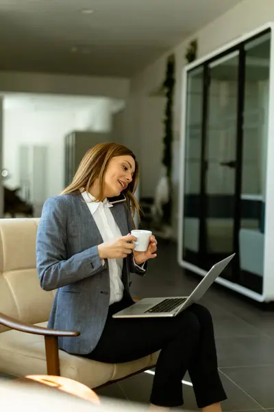 Elbiseleri Içindeki Bir Kadın Telefonda Konuşurken Kahvesini Yudumluyor Bilgisayarı Günlük — Stok fotoğraf
