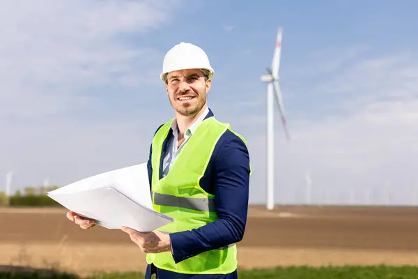 Cheerful Man Safety Gear Scrutinizes Blueprints Windmills Towering Background — Stock Photo, Image