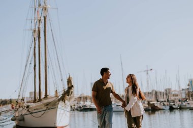 Cuple, Barcelona 'daki sakin marinada demirli teknelerin yanında huzurlu bir yürüyüşün tadını çıkarıyor. Sabah güneşinin tadını çıkarıyor..