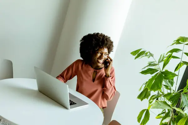 쾌활한 여자는 그녀의 노트북과 활기찬 식물과 테이블에서 그녀의 전화에 이야기 로열티 프리 스톡 사진