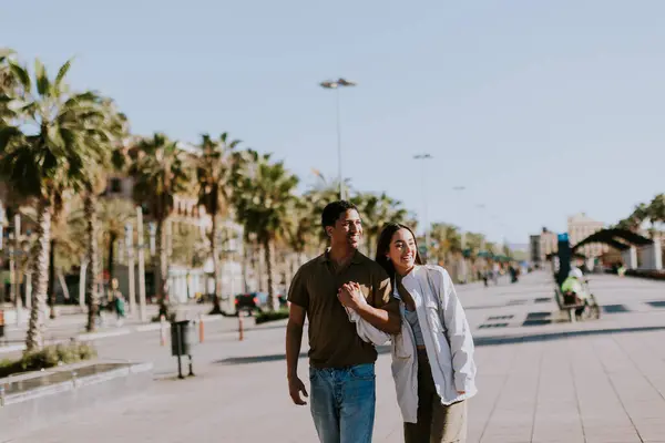 在巴塞罗那 一对年轻夫妇手牵着手 微笑着走在一条阳光灿烂的小径上 两边都是手掌 图库图片