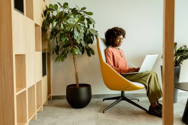 Ruhani Afrikalı Amerikalı iş kadını laptopuyla çalışırken gülümsüyor, rahat bir ofis salonunda oturuyor..