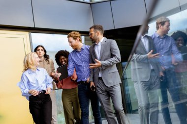 Bir grup iş arkadaşı, gün sona ererken yansıtıcı cam cephede fikirlerini paylaşıyorlar..