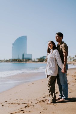 Gülümseyen bir çift kumlu bir sahilde kaygısızca koşmaktan hoşlanır, arka planda yavaşça dalgalar kırılır.