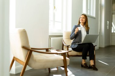 Dizüstü bilgisayarıyla uğraşırken kahvesini yudumluyor, gün ışığında güneşleniyor..