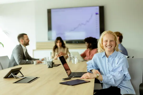 Fröhliche Geschäftsfrau Mit Laptop Lächelt Die Kamera Während Kollegen Hintergrund lizenzfreie Stockfotos