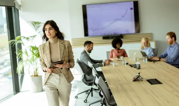 Determined Female Leader Stands Foreground Tablet Addressing Her Attentive Team Stock Image