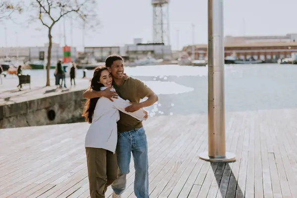 楽しいカップルはバルセロナの桟橋で抱擁し 街のスカイラインはバックグラウンドで柔らかくぼやけます ロイヤリティフリーのストック画像