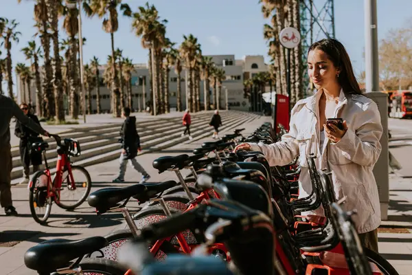 Fiatal Áll Egy Sor Piros Kerékpár Napsütötte Barcelona Ellenőrzi Telefonját Stock Fotó