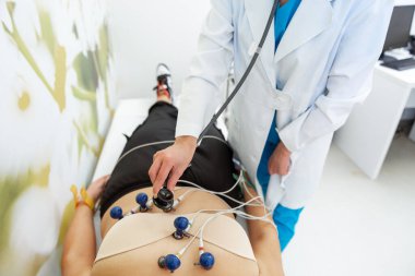 Bir tıbbi uzman ECG testini dikkatlice uygularken bir hasta rahatlar..