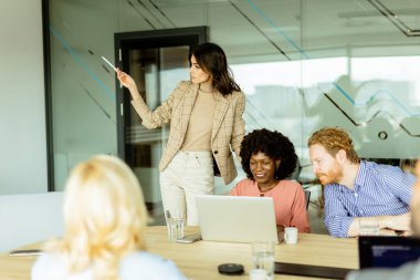 İş kadını, finans toplantısı sırasında ekrandaki büyüme eğilimlerine işaret ederken, katılımcılar dikkatle dinliyor