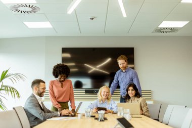 Bir grup profesyonel dizüstü bilgisayarın etrafında toplanarak parlak bir ofis ortamında fikir alışverişinde bulundu..