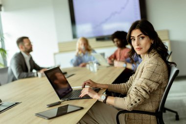 Kendine güveni tam bir iş kadını, modern ofis ortamında başarıyı ve takım çalışmasını yansıtan bir gülüşü var..
