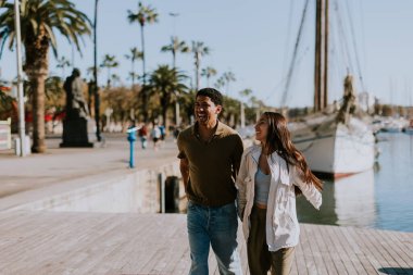 Cuple, Barcelona 'daki sakin marinada demirli teknelerin yanında huzurlu bir yürüyüşün tadını çıkarıyor. Sabah güneşinin tadını çıkarıyor..