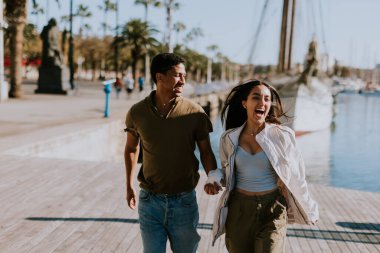Cuple, Barcelona 'daki sakin marinada demirli teknelerin yanında huzurlu bir yürüyüşün tadını çıkarıyor. Sabah güneşinin tadını çıkarıyor..
