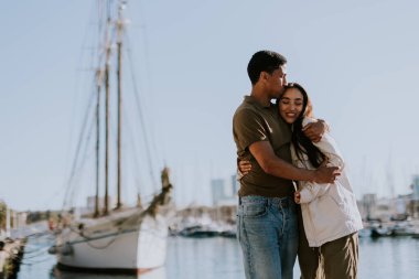 Cuple, Barcelona 'daki sakin marinada demirli teknelerin yanında huzurlu bir yürüyüşün tadını çıkarıyor. Sabah güneşinin tadını çıkarıyor..