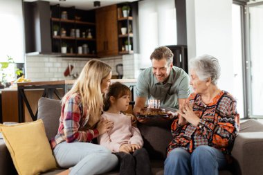 Mutlu bir büyükanneye doğum günü pastası sunmak için kanepenin üzerinde toplanan çok nesilli bir ailenin anılarını canlandırması iç açıcı bir sahne.