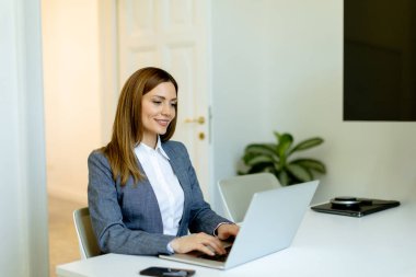 Odaklanmış profesyonel kadın dizüstü bilgisayarı üzerinde özenle çalışıyor, çalışma alanı doğal ışıkla yıkanıyor..