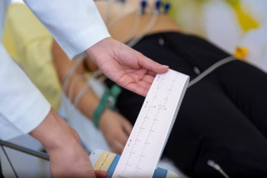 Bakıcı elinde EKG 'si olan bir hastanın hayati değerlerini dikkatle kontrol ediyor..