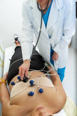 Bir tıbbi uzman ECG testini dikkatlice uygularken bir hasta rahatlar..