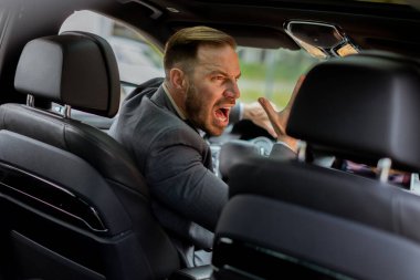 Trafik sıkışıklığında direksiyon başında bağıran takım elbiseli kızgın bir adam.