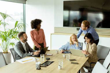 Bir grup profesyonel dizüstü bilgisayarın etrafında toplanarak parlak bir ofis ortamında fikir alışverişinde bulundu..
