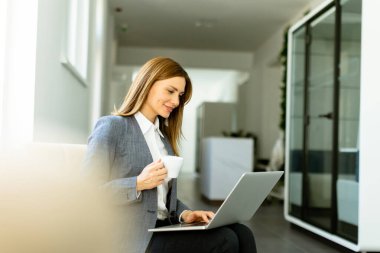 Dizüstü bilgisayarıyla uğraşırken kahvesini yudumluyor, gün ışığında güneşleniyor..