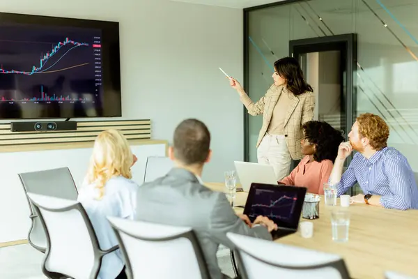 Businesswoman Points Growth Trends Screen Financial Meeting Attendees Listening Intently Stock Photo