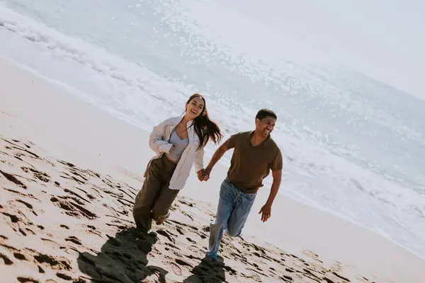 一对笑容满面的夫妻在沙滩上无忧无虑地奔跑着 背景中的波浪轻轻荡漾 免版税图库图片