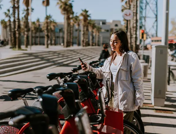 若い女性は晴れたバルセロナで赤い自転車の列に立って 携帯電話をチェックし バイクシェアリングアプリを使用する可能性が高い ストック写真