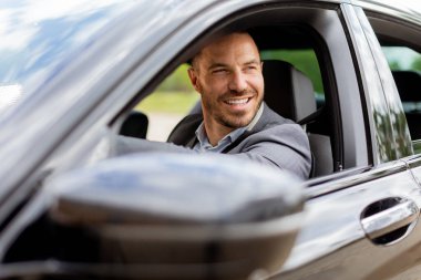 Neşeli sürücü direksiyonu tutarken gülümser, iyi donanımlı bir araçla yolda ilerler.