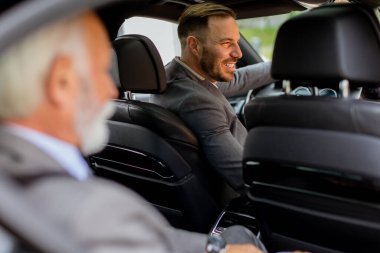 Neşeli adam bir aracın arka koltuğunda oturur, şoförle dostluk anını paylaşır.