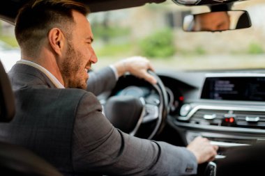 Neşeli sürücü direksiyonu tutarken gülümser, iyi donanımlı bir araçla yolda ilerler.