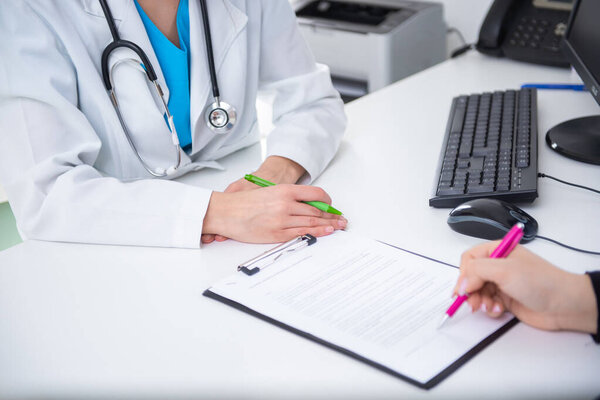 Female doctor in a white coat with a stethoscope advises a patient, who is taking notes in an office setting — Stock Image Female Doctor White Coat Stethoscope Advises Patient Who Taking Notes Stock Image