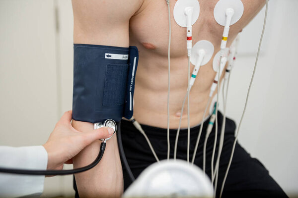 A patient is being examined with EKG leads attached, while a health professional measures blood pressure. — Stock Image Patient Being Examined Ekg Leads Attached While Health Professional Measures Royalty Free Stock Images