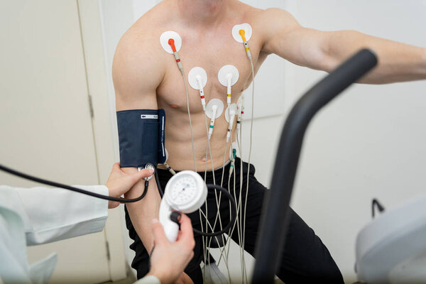 A patient is being examined with EKG leads attached, while a health professional measures blood pressure. — Stock Image Patient Being Examined Ekg Leads Attached While Health Professional Measures Royalty Free Stock Images