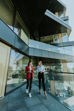 İki profesyonel kadın gündüz vakti gösterişli, çağdaş bir ofis binasının dışındaki tableti incelerken düşünceli bir tartışmaya giriyorlar..
