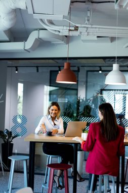 Çağdaş bir ofis ortamında, son moda aydınlatma ve geniş pencerelerle tamamlanmış, parlak ve üretken bir atmosfer yaratan bir tartışmaya giren iki kadın..