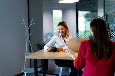 Çağdaş bir ofis ortamında, son moda aydınlatma ve geniş pencerelerle tamamlanmış, parlak ve üretken bir atmosfer yaratan bir tartışmaya giren iki kadın..