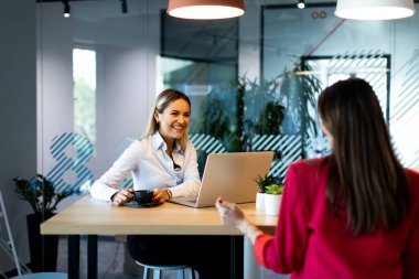 Çağdaş bir ofis ortamında, son moda aydınlatma ve geniş pencerelerle tamamlanmış, parlak ve üretken bir atmosfer yaratan bir tartışmaya giren iki kadın..